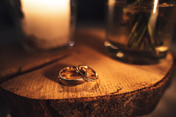 Pair of decorated wedding rings laying on wood. Warm tones by candle light. Shallow depth of field. Orange toned.