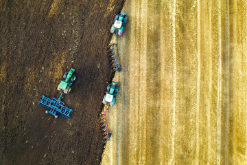 Aerial view of a tractor plowing black agriculture farm field after harvesting in late autumn.