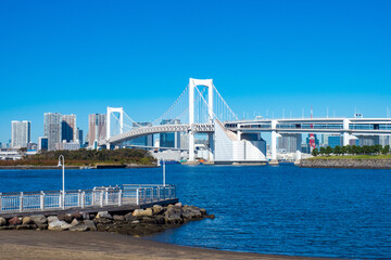 Wall Mural - Japan. Rainbow bridge and Wharf in Tokyo Bay. Blue water of Tokyo Bay against the blue sky. Panorama of Odaiba island. Guide to Tokyo. White suspension bridge in the capital of Japan.