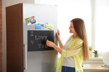 Sticker - Young woman writing text I LOVE YOU on chalkboard in kitchen