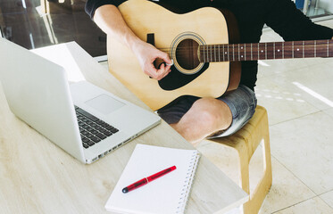 man learning to play guitar online using laptop