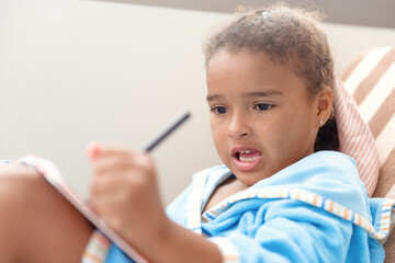 Little girl drawing at home sitting on chair.