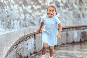 Happy beautiful girl running through the spray of water.