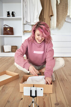 Happy hipster gen z teen girl fashion social media channel blogger pink hair wear hoodie record unboxing vlog on phone video camera tutorial sit on floor open online store clothes order box, vertical.