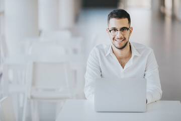 Positive recruiter wearing elegant clothes sitting at a desk with a laptop, waiting for a job candidate