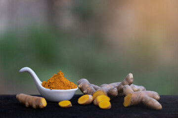 fresh turmeric root and turmeric powder in spoon on wooden background