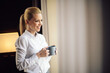 © JustLife - Businesswoman relaxing in hotel room. Young beautiful woman drinking coffee.