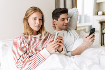 Poster - Portrait of happy couple smiling and using smartphones while lying