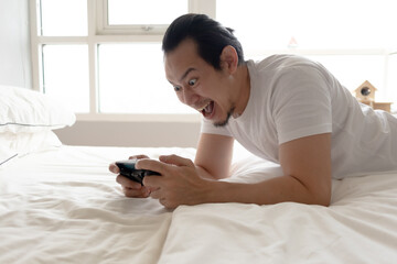 Happy Asian man stays home and play mobile game in his apartment.