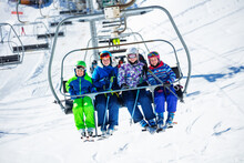Group Of Skiers Children Sit On Chairlift Going On The Mountain To Ski, Sitting Together Smiling