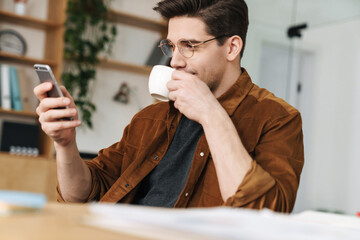 Sticker - Image of joyful man smiling and using cellphone while drinking coffee