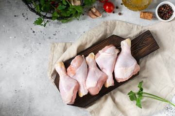 Wall Mural - A chicken drumstick on a wooden Board on the light gray kitchen table. Raw chicken drumstick in the process of cooking. Chicken leg. The view from the top