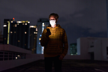 Poster - Young man with mask thinking while using phone against view of the city at night