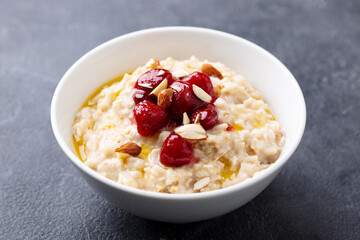 Wall Mural - Oatmeal porridge with strawberry jam in white bowl. Grey background. Close up.