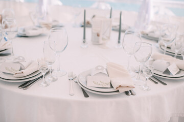 Wall Mural - Restaurant, banquet, table setting. The table is covered with a white tablecloth, dishes, white clean plates, cutlery, napkins, wine glasses, candles. Close-up.