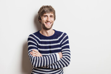 Portrait of handsome smiling young man with folded arms. Smiling joyful cheerful men with crossed hands studio shot. Isolated on gray background