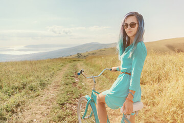 Sticker - Beautiful woman sits on bicycle on country road along green meadows.