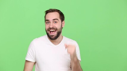 Wall Mural - Bearded young guy 20s in white t-shirt isolated on green chroma key background studio. People sincere emotions lifestyle concept. Dancing fooling around having fun expressive gesticulating with hands