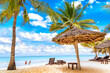 Sun loungers under umbrella and palms on the sandy beach by the ocean and cloudy sky. Vacation background. Idyllic beach landscape in Diani beach, Kenya, Africa