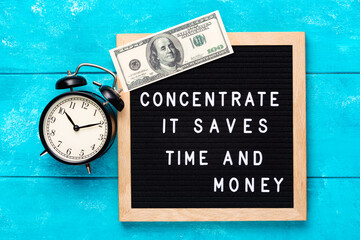 Poster - Inspirational motivational business quote Concentrate. It Saves Time and Money words on blue letter board with hundred dollar bill on wooden background near vintage alarm clock. Motivation concept.