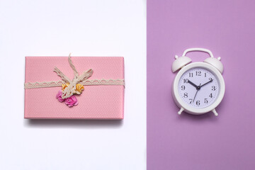 pink gift box wrapped with vintage ribbon on a light background and a white alarm clock on a pink 