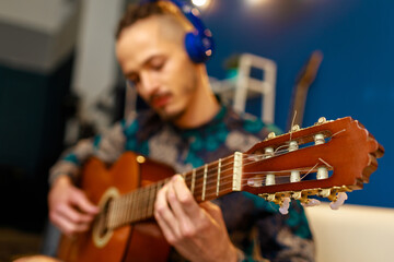 Wall Mural - Young caucasian man with dreadlocks sitting on sofa and playing acoustic guitar