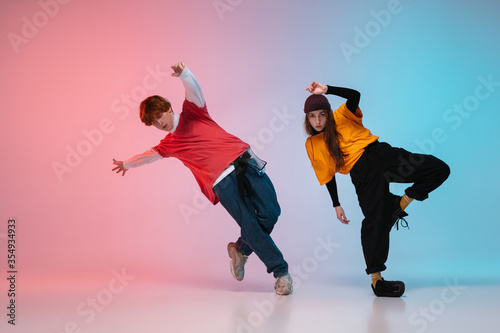 Fototapeta na szkło Boy and girl dancing hip-hop in stylish clothes on colorful gradient background at dance hall in neon. Youth culture, movement, style and fashion, action. Fashionable bright portrait. Street dance.