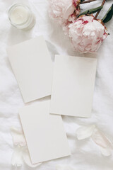 Wall Mural - Wedding stationery, still life composition. Greeting cards mockup scene. Blank sheets of paper and pink peony flowers on white linen table cloth. Vintage feminine styled photo, flat lay, top view,