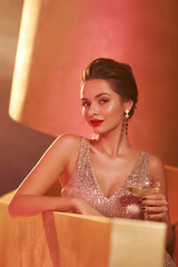 Elegant stylish woman with hairstyle having fun at luxury party at night club. Stunning girl in golden sequins sexy dress with glass of champagne. Lady relaxing. Closeup portrait