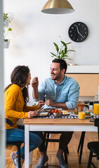 Wall Mural - Smiling man feeding happy woman stock photo. Wife and husband eating breakfast together 