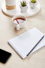Wall Mural - green plants, cup of tea and blank notebook with pencil near smartphone on wooden surface