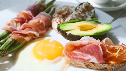 Wall Mural - fried asparagus wrapped in jamon, fried eggs, bruschetta with soft cheese and avocado on a white plate and a cup of freshly brewed coffee