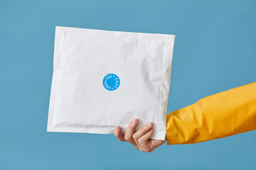 Close-up of female hand holding parcel packed in white paper isolated on blue background