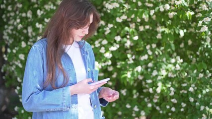 A beautiful girl ties her card to her phone by scanning qr code on it. A woman with a phone on the street against the background of flowers