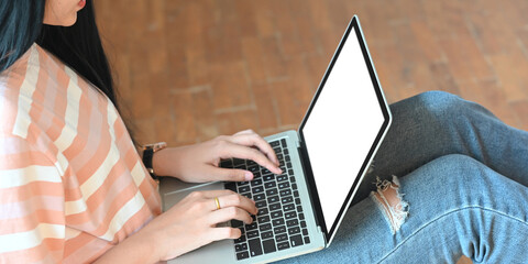 Cropped image of creative woman hands using a computer with white bank screen that putting on her lap over comfortable sitting room as background.