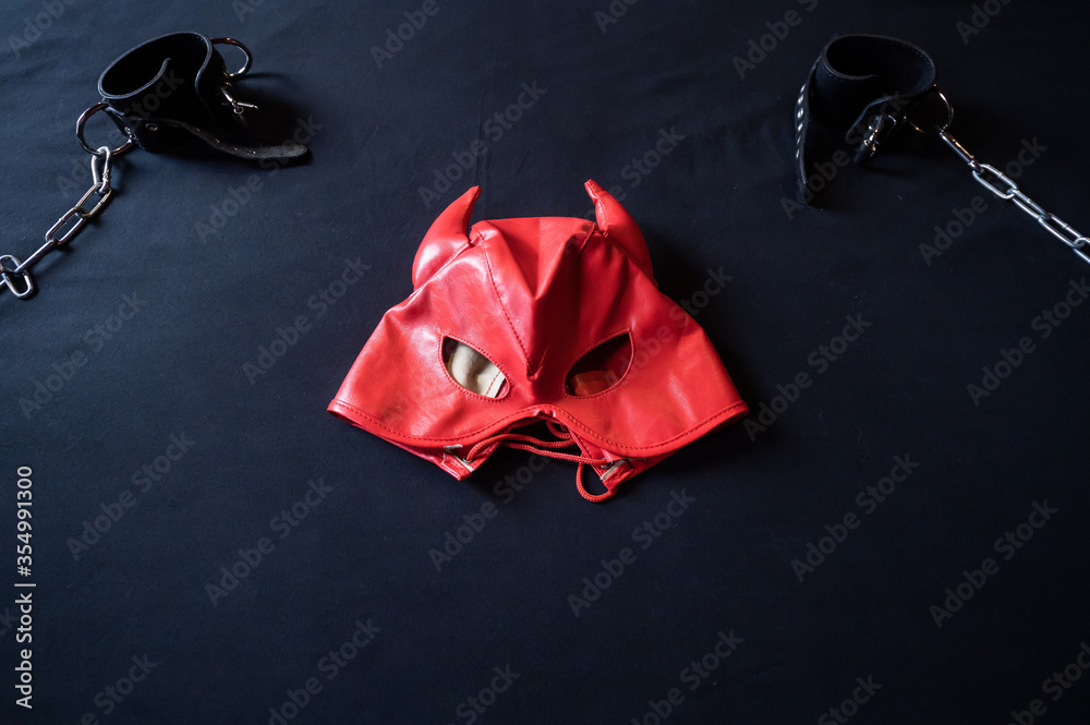 BDSM equipment. Top view of a red leather devil mask and black handcuffs  with chains on a gray sheet. Sex toys. Dominance. No people. Stock Photo |  Adobe Stock