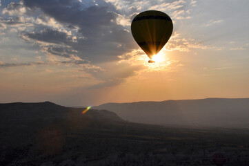  Hot air balloon silhouette against the sun and clouds at sunrise, with sun rays and flares, over Cappadocia, Turkey