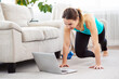 © Admiral - Online home fitness. Slim girl doing workout routine on floor and watching laptop at home. Copy space