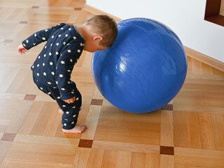 child plays with a big blue ball. Developing motor skills. Baby plays