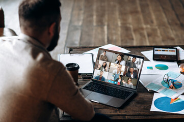 Wall Mural - App for communication with employees. Online video conference. Young bearded man communicates via video call with colleagues, he sits at the creative modern office space