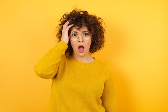 Embarrassed attractive Arab female with shocked expression, dressed in yellow sweater, expresses great amazement, isolated over yellow background. Puzzled man poses indoor