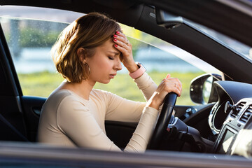 Exhausted woman driver feeling headache, sitting inside her car, keeping hand to head and feeling anxiety. Stop after driving car in traffic jam.Blood pressure