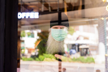 Sticker - Mature bearded hipster man with mask using phone at the coffee shop through the window