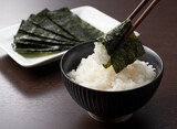 Fototapeta  - Wrapping nori around rice set against a wooden backdrop.