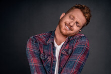 Silly And Funny Caucasian Redhead Guy With Bristle, Tilting Head And Leaning On Shoulder With Lovely And Cute Expression, Smiling With Closed Eyes Being Tender And Girly Over Gray Background