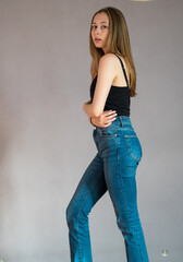 Wall Mural - Full body portrait of a pretty teenage girl wearing a black tank top and denim jeans standing looking at the camera. Studio shot