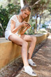 © JackF - Teenage  girl  using phone sitting at stone  bench in park at summer day