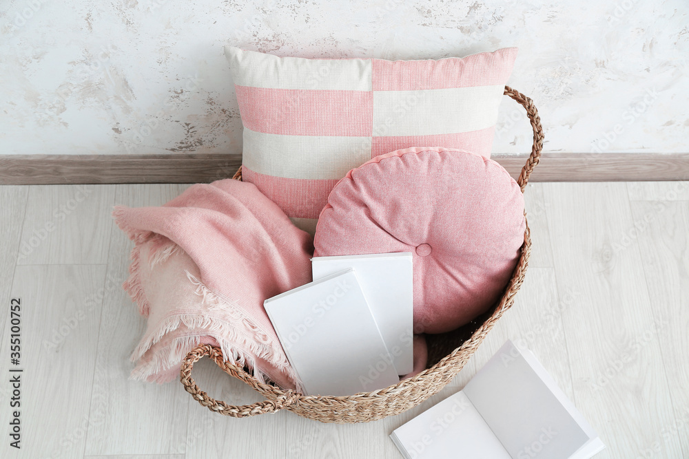 Wicker basket with pillows, plaid and books in room