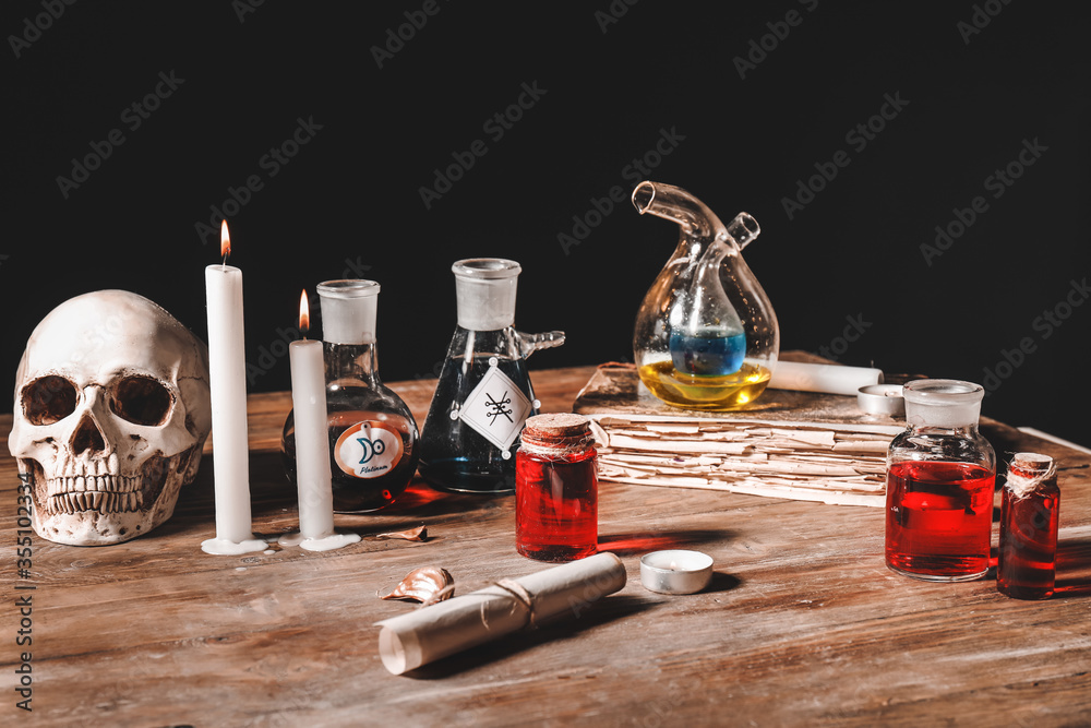 Potions, human skull, old book and candles on alchemist's table