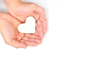 Cupped hands holding a white heart in white background. Charity, pure love, compassion and kindness concept. Top view.